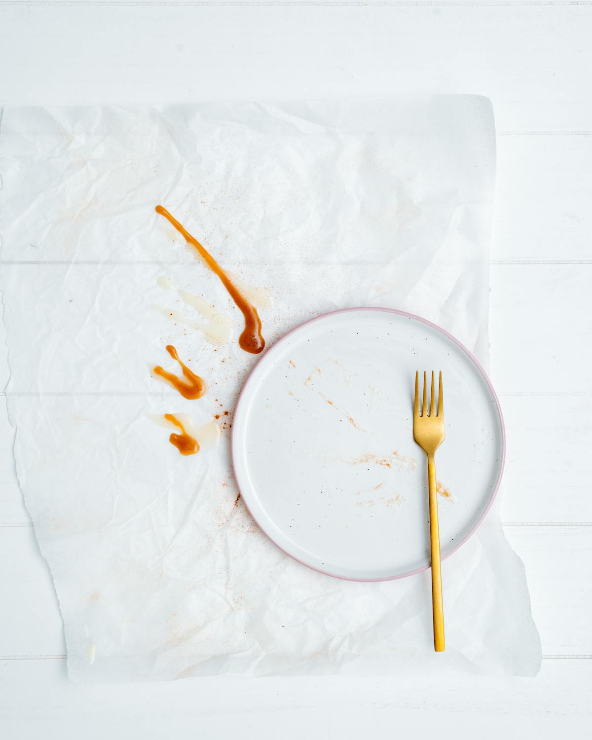 A gold fork resting on an empty white plate on a sunlit table — a quiet image for thinking about how we relate to food and eating