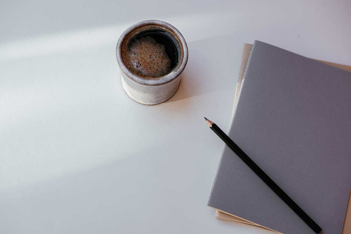 A ceramic cup of coffee, a grey notebook and a pencil on a sunlit desk — a quiet moment for thinking about therapy as a private investment